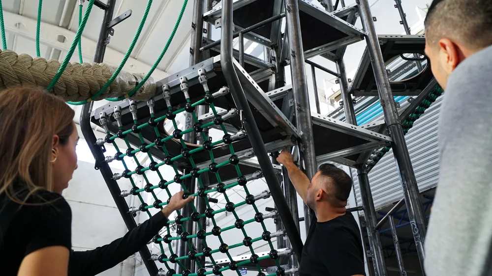 Team assembling the steel play structure with green nets in the workshop