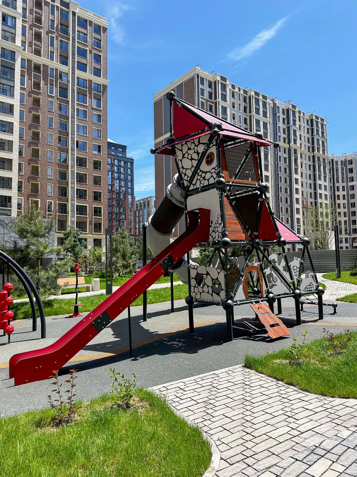 Red and grey climbing tower with a tube slide in a residential courtyard, Kazakhstan